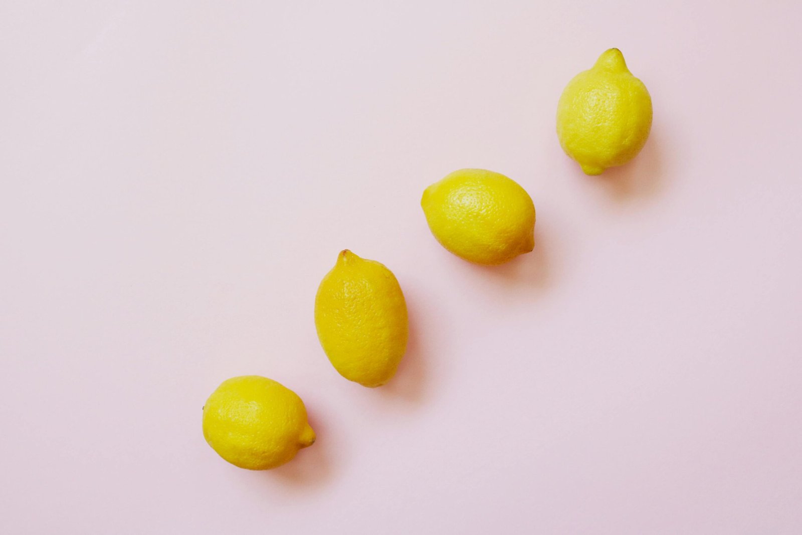 A minimalist display of vibrant lemons lined against a pastel pink surface, creating a fresh and juicy vibe.